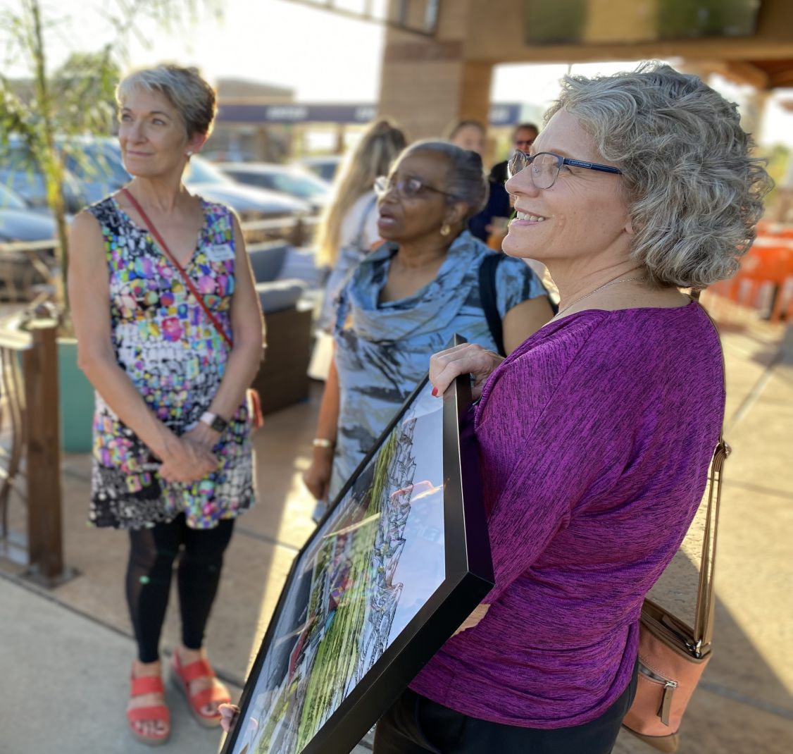 Women at a community event, one holding a framed poster