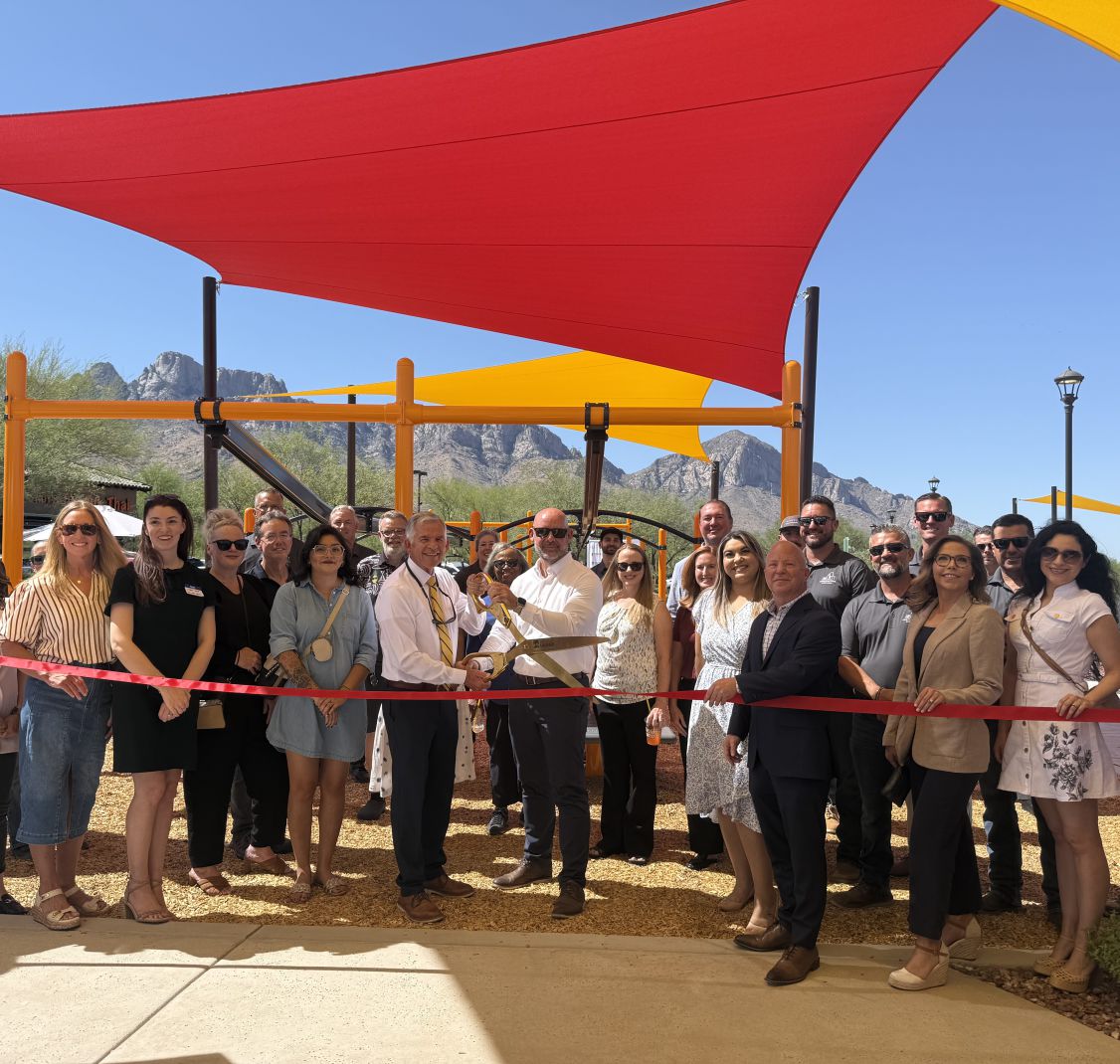 A group cutting a red ribbon under shade sails at a playground