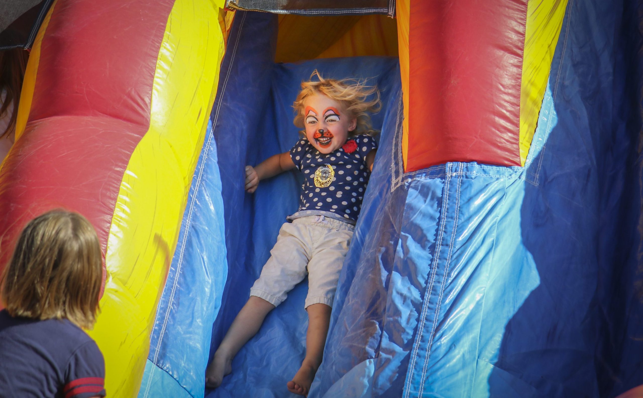 A child with a painted face coming down an inflatable slide