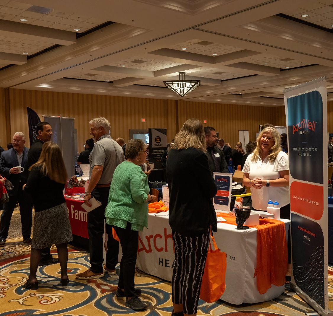 Visitors talking with exhibitors at tables in a hotel ballroom
