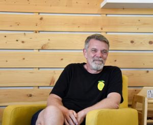 A man sitting in a yellow armchair in front of a wood-panelled wall